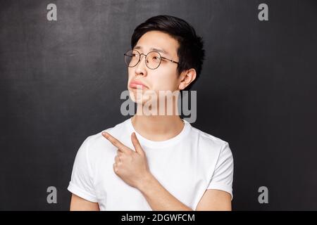 Primo piano ritratto di geloso e cupo giovane asiatico si sentono rimpienti, guardare qualcosa di sconvolgimento, pointing puntando il dito a sinistra, Foto Stock
