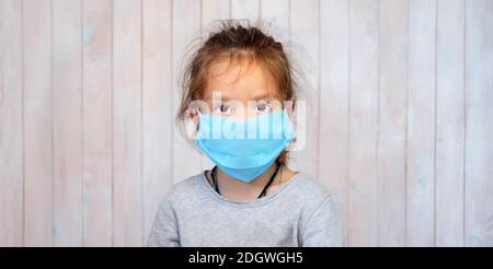Bambina in maschera medica. Bambini e Coronavirus. Ragazza di cinque anni che indossa la maschera guardando la fotocamera. Ritratto di bella ragazza in maschera medica Foto Stock
