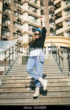 Donna elegantemente vestita con jumpsuit in denim blu in posa con skateboard. Via foto. Ritratto di ragazza che tiene skateboard. Massima vita Foto Stock