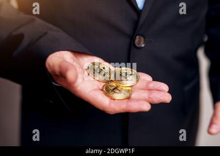 Primo piano di un uomo d'affari maturo in tuta mani che tengono tre bitcoins.s Foto Stock