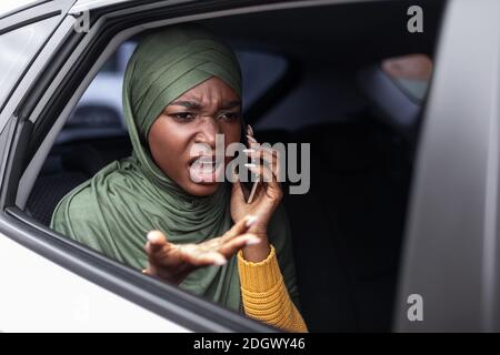 Dispiaciuta donna musulmana nera che parla su Cellphone su Backseat in Auto Foto Stock