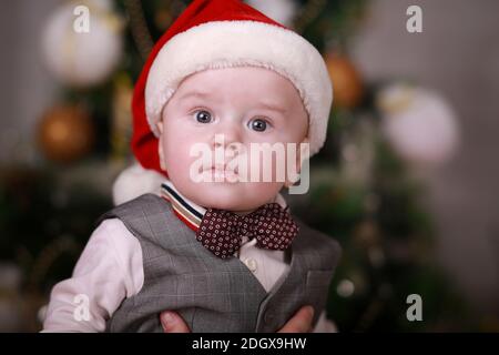 Divertente bambino ragazzo indossato in cappello di Santa con sullo sfondo albero di natale. Foto Stock