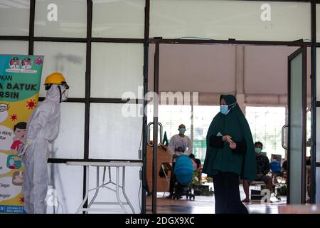 Un paziente COVID-19 lancia il suo scrutinio mentre un ufficiale sanitario rivestito in tuta di nocciolo guarda a una struttura di isolamento COVID-19, che ospita 49 elettori, a South Tangerang, Banten Foto Stock