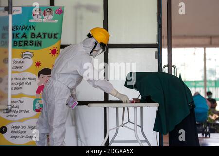 Un paziente COVID-19 lancia il suo scrutinio mentre un ufficiale sanitario rivestito in tuta di nocciolo guarda a una struttura di isolamento COVID-19, che ospita 49 elettori, a South Tangerang, Banten Foto Stock