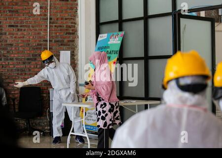 Un paziente COVID-19 lancia il suo scrutinio mentre un ufficiale sanitario rivestito in tuta di nocciolo guarda a una struttura di isolamento COVID-19, che ospita 49 elettori, a South Tangerang, Banten Foto Stock