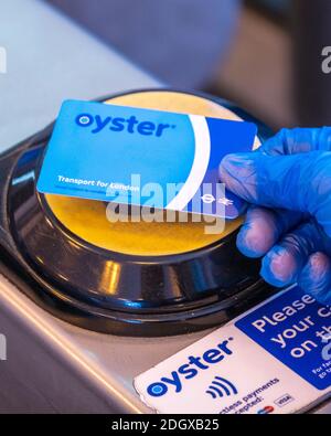 Una mano che indossa un guanto ospedaliero in vinile protettivo con un Toccare e pagare la smart card (Oyster card) Per aprire un cancello sulla metropolitana di Londra Foto Stock