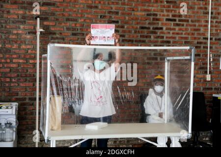 Un paziente COVID-19 lancia il suo scrutinio mentre un ufficiale sanitario rivestito in tuta di nocciolo guarda a una struttura di isolamento COVID-19, che ospita 49 elettori, a South Tangerang, Banten Foto Stock