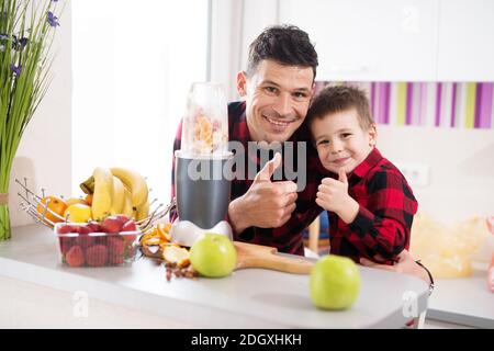 Padre e figlio nella stessa camicia stanno dando un pollice in su insieme mentre attendono un frullatore per finire di fare i loro frullati. Foto Stock