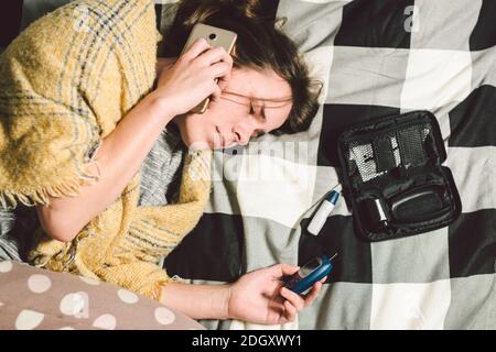 Tema diabete. Giovane donna casa camera da letto letto utilizza il dispositivo di tecnologia che misura i livelli di glucosio nel sangue, glucometro test strips alto Foto Stock