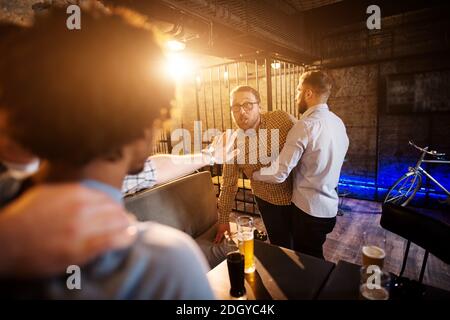 Amici che impediscono la lotta e la difficoltà di due ragazzi pazzi al bar. Foto Stock