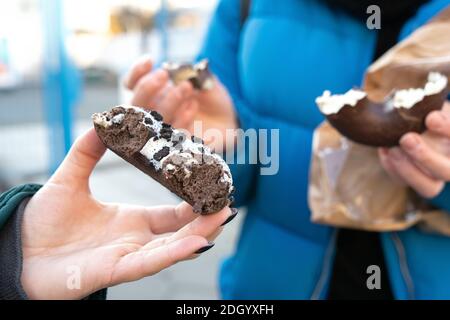 Mani femminili con gustosa ciambella choco nella vita reale Foto Stock