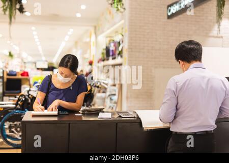 Donna in maschera protettiva firma documenti al banco cassa nel centro commerciale. Foto Stock