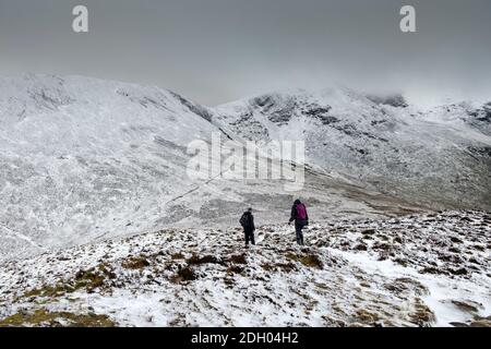 Due camminatori discendenti dalla cima del outerside con la neve coperta montagna di Sail Beyond, Lake District, Cumbria, UK Foto Stock