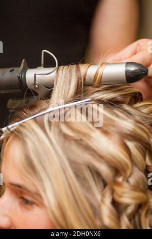 Parrucchiere arricciando i capelli di una donna bionda Foto Stock