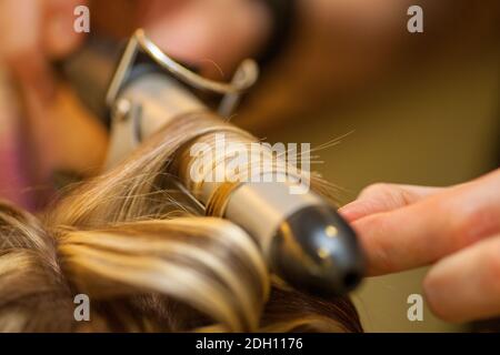 Parrucchiere arricciando i capelli di una donna bionda Foto Stock