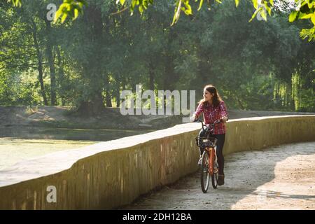 Oggetto trasporto ecologico in bicicletta. Giovane caucasica che cavalca su una strada sterrata in un parco vicino ad un lago che affitta un colore arancio Foto Stock
