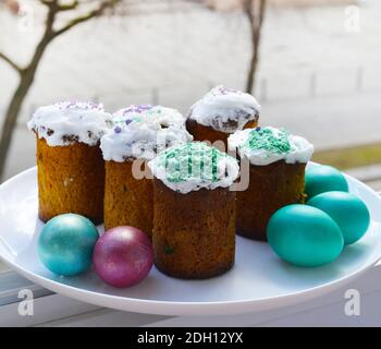 Piccole torte pasquali e uova colorate su un piatto bianco alla finestra. Pasqua in città. Foto Stock
