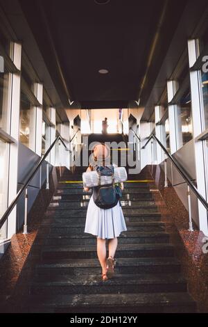 Giovane bella donna caucasica turistica in un abito estivo e. cappello con uno zaino turistico sale la donna estiva sulla rotaia Foto Stock