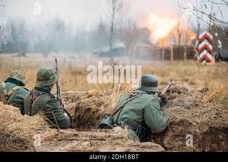 Re-enactor vestiti come soldati tedeschi della fanteria Wehrmacht durante la guerra mondiale II Nascosto seduta con armi di fucili in un imboscamento in Trincea Foto Stock