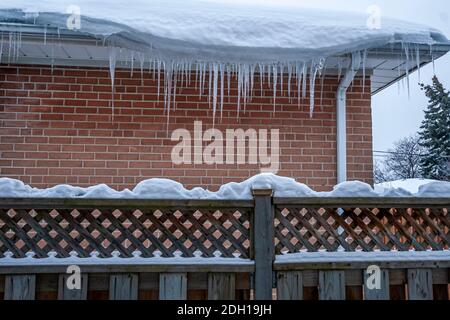 Scena invernale - Casa tetto coperto di neve fresca con picchetti di ghiaccio appesi sul lato del tetto dopo una neve tempesta Foto Stock