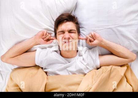 Dispiaciuto Young Man tappare le orecchie nel letto a. La casa Foto Stock