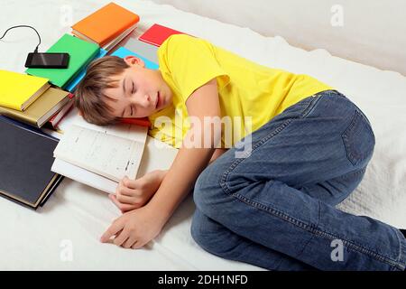 Il ragazzo stanco dorme con i libri sul letto a. La casa Foto Stock