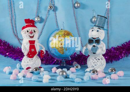 Due simpatici pupazzi di neve in abiti blu e rossi si trovano sul palcoscenico blu di Capodanno, e tra di loro c'è il globo Foto Stock