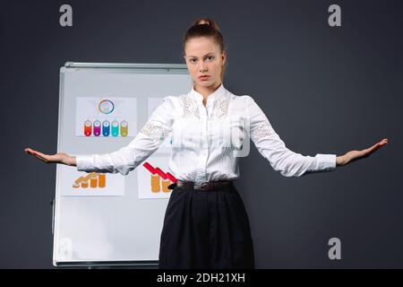 La giovane boss ha allargato le braccia ai lati durante la conferenza. Diagrammi aziendali. Foto su sfondo grigio. Foto Stock