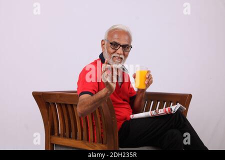Felice anziano indiano che beve o tiene un bicchiere di succo d'arancia o di mango fresco Foto Stock