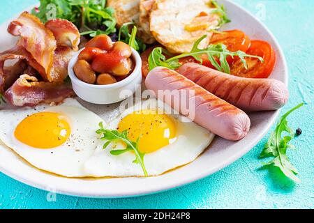 Colazione all'inglese: Uova fritte, fagioli, pomodori, salsiccia, pancetta e pane tostato. Foto Stock
