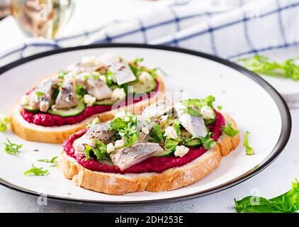 Filetto di aringa. Insaporire con aringhe salate e pate di barbabietole sulle tostature su piastra bianca. Cucina scandinava. Foto Stock
