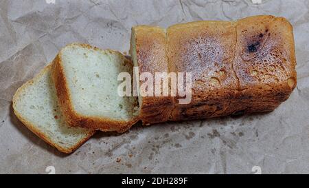 foto ravvicinata di pane appena sfornato parzialmente tagliato su un foglio di carta kraft. foto a fuoco selettivo di pane parzialmente tagliato. Foto Stock