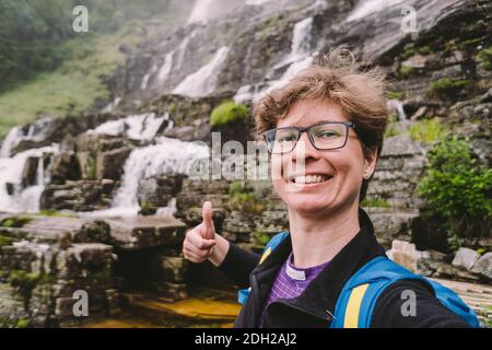 Woman tourist fa selfie foto sullo sfondo di Tvindefossen o Tvinnefossen cascata vicino Voss, Norvegia. Naturale, paesaggio. Foto Stock