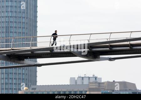 Vista ad angolo basso di un corridore che si esercita sul Millennium Bridge con grattacieli sullo sfondo, Londra Foto Stock