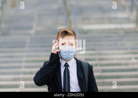 Scolaro esce dalla scuola indossando una maschera protettiva nel città Foto Stock