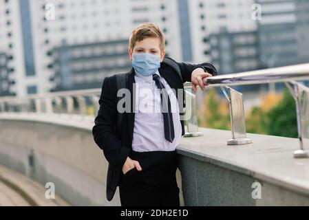 Scolaro esce dalla scuola indossando una maschera protettiva nel città Foto Stock