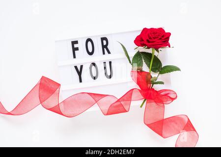 San Valentino, amore, concetto romantico. Fiori di rosa rosso fresco con nastro e testo per voi su scatola luminosa su sfondo bianco. Biglietto d'auguri. Posa piatta, Foto Stock
