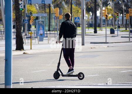 Vista posteriore di un giovane con uno scooter elettrico in una strada. Foto Stock
