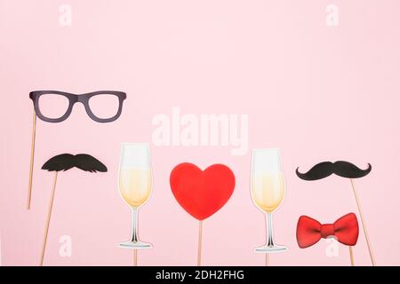 San Valentino lgbt, amore, concetto romantico. Cuore rosso, bicchieri di champagne con baffi di carta di coppia su sfondo rosa. Biglietto d'auguri. Piatto la Foto Stock