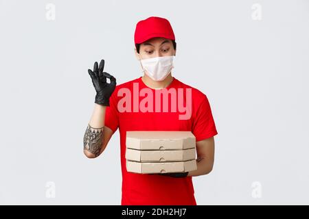 Uniforme rossa, cappuccio e t-shirt, indossando guanti protettivi e maschera medica per la sicurezza del cliente durante la consegna Foto Stock