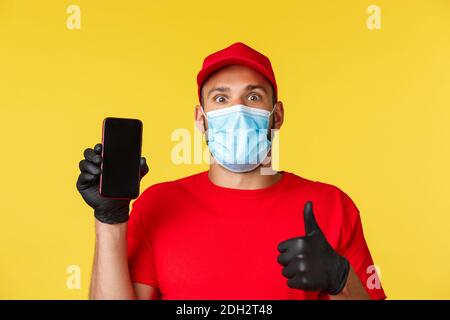 Covid-19, ordini di consegna, shopping, contactless payment e social distancing concetto. Dipendente eccitato, corriere in uniforme rossa Foto Stock