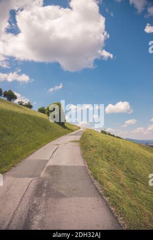 Asphalted steep mountain road on an Austrian mountain. Blue sky and green meadow, summer time Foto Stock