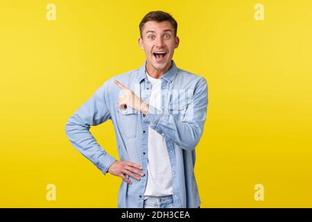 Entusiasta felice bell'uomo biondo in outfit elegante, puntando dito in alto a sinistra angolo e sorridendo ampiamente, scoperto stupin Foto Stock