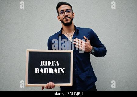 Uomo arabo indossare camicia blu e occhiali tenere tavola con l'iscrizione Riffa Bahrain. Le città più grandi del mondo islamico concetto. Foto Stock