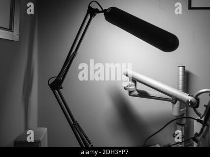 Immagine monocromatica in bianco e nero della lampada da tavolo articolata con le braccia nere in primo piano si sfuocano e il supporto per monitor articolato Foto Stock