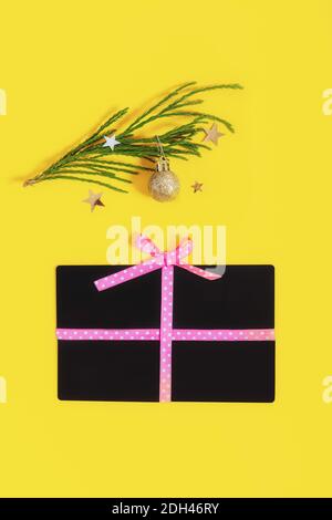 Forma piatta della scatola del regalo della disposizione con un arco fatto delle giftcards del negozio e delle sfere dorate ramo dell'albero di natale sul colore giallo di tendenza sfondo. Idee creative Foto Stock