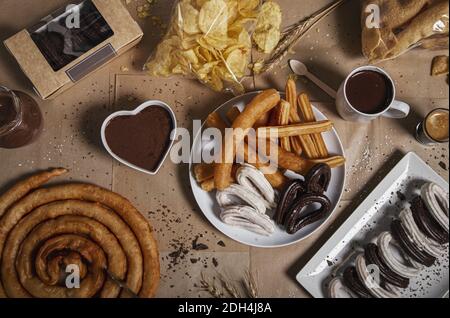 La varietà di churros tradizionali con zucchero granulato e cioccolato su un fondo di carta artigianale. Foto Stock