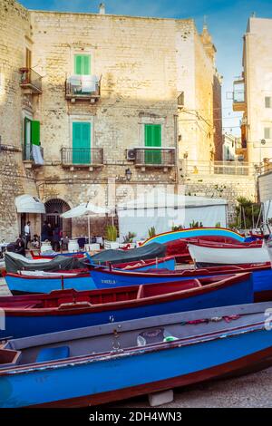 Giovinazzo, Italia: Colorate vecchie barche da pesca in legno ormeggiate nel porto della città vecchia; la piazza di fronte al ristorante nella torre di difesa Foto Stock