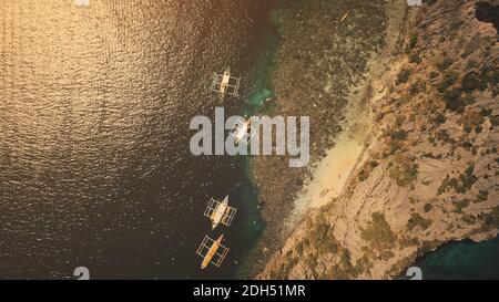 In cima alle tradizionali barche per passeggeri delle Filippine con vista aerea al tramonto. Trasporto di acqua alla baia dell'oceano con la costa della spiaggia di sabbia dell'isola di montagna di Palawan. Spettacolare blu marino scuro Foto Stock