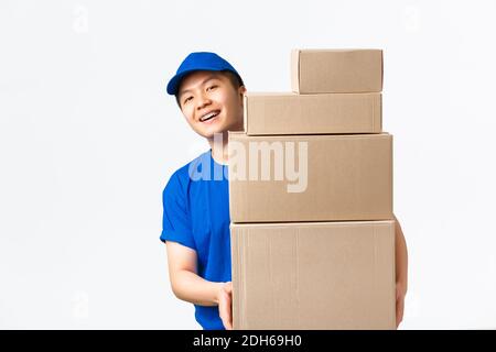 Shopping online, concetto di spedizione rapida. Sorridente felice asiatico consegna uomo in uniforme blu corriere, guardando dietro le scatole con clie Foto Stock